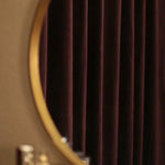 Miroir rond au cadre doré devant un rideau sombre, idéal pour une décoration élégante et moderne. Parfait pour ajouter une touche sophistiquée à votre intérieur.