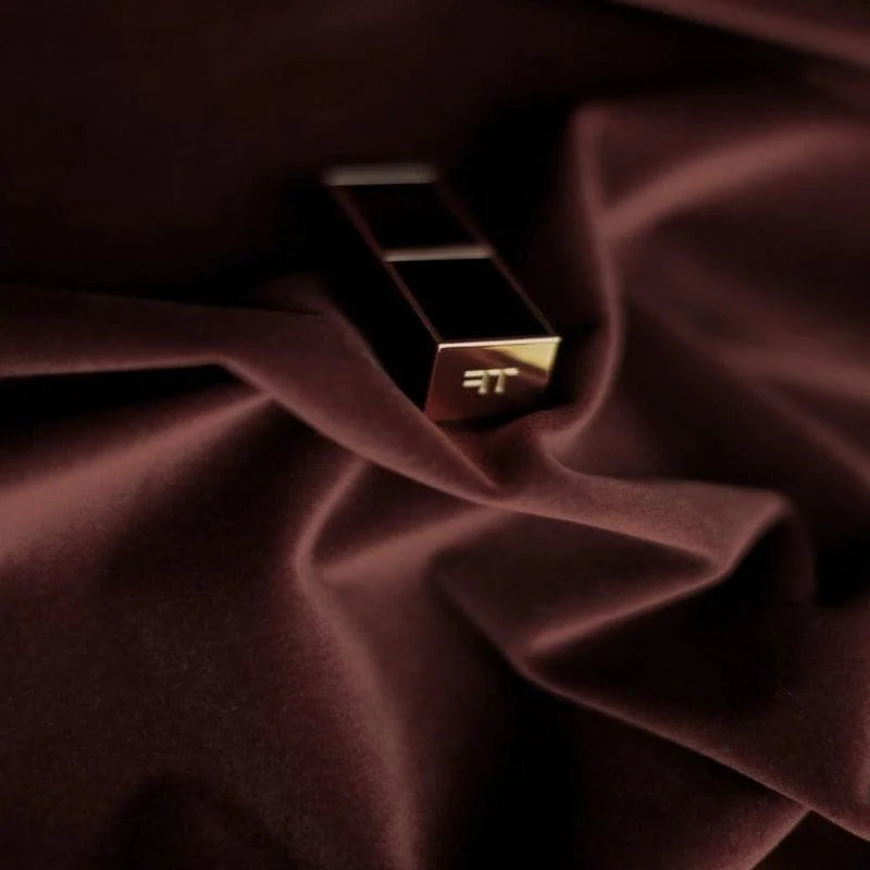 Rouge à lèvres de luxe posant sur un tissu brun foncé, avec un design élégant et moderne. Le tube doré reflète une lumière douce, soulignant son esthétique raffinée. Accessoire de maquillage incontournable pour un look sophistiqué.