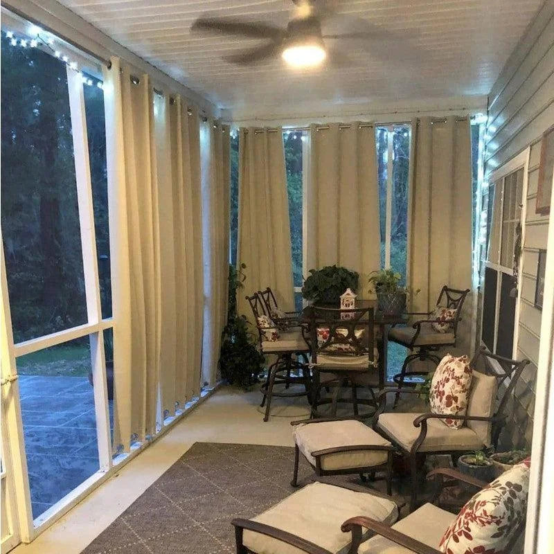 Véranda élégante avec rideaux opaques pour une intimité maximale. Aménagement confortable incluant fauteuils et table accompagnés de coussins décoratifs. Lumières d'extérieur créant une ambiance chaleureuse pour des soirées conviviales. Idéal pour profiter d'un espace extérieur protégé tout au long de l'année.