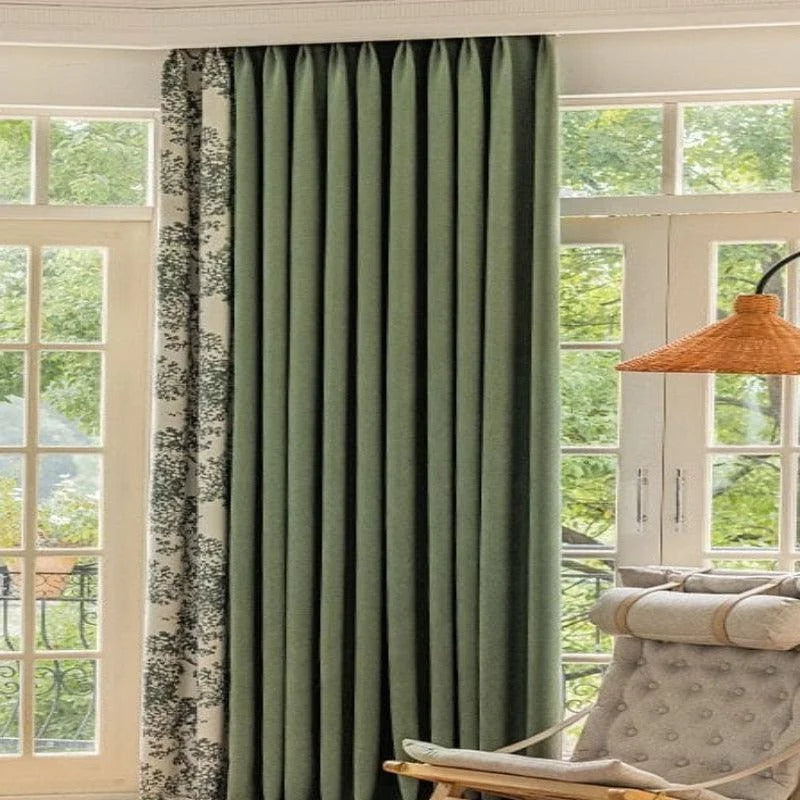 Rideau de couleur vert foncé suspendu près d'une grande baie vitrée, apportant élégance et ambiance naturelle à un salon lumineux. Accessoire idéal pour contrôler la lumière et ajouter une touche de sophistication à la décoration intérieure.
