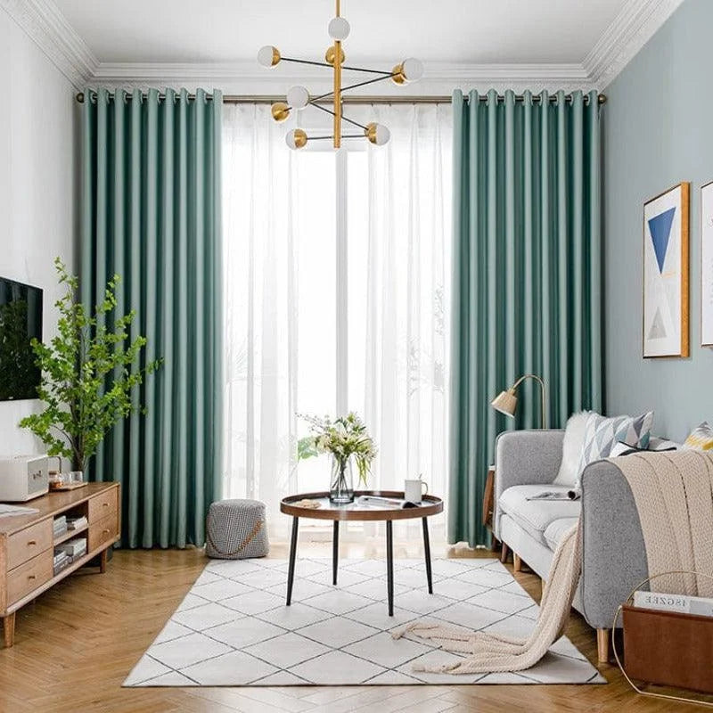 Salon moderne avec canapé gris et rideaux vert foncé, tapis à motifs géométriques et table basse ronde en bois. Plafonnier design doré, décoration élégante avec plantes vertes et cadres muraux artistiques. Intérieur lumineux et accueillant.