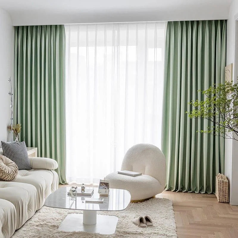 Salon moderne avec rideaux élégants, vert pastel, profitant d'une belle lumière naturelle. Décoration intérieure chic avec canapé confortable et fauteuil design, créant une ambiance chaleureuse et accueillante. Sol en bois clair et tapis moelleux ajoutant une touche cosy. Idéal pour un espace de détente raffinée.