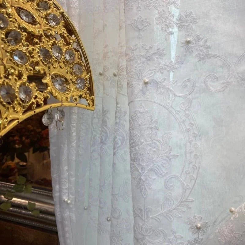 Rideau décoratif blanc avec motifs brodés élégants et perles, idéal pour salon ou chambre à coucher, apportant une touche de luxe et de sophistication à tout intérieur. Fond de miroir classique et éventail doré, embellissant l'espace avec charme et lumière. Parfait pour une décoration raffinée et contemporaine.