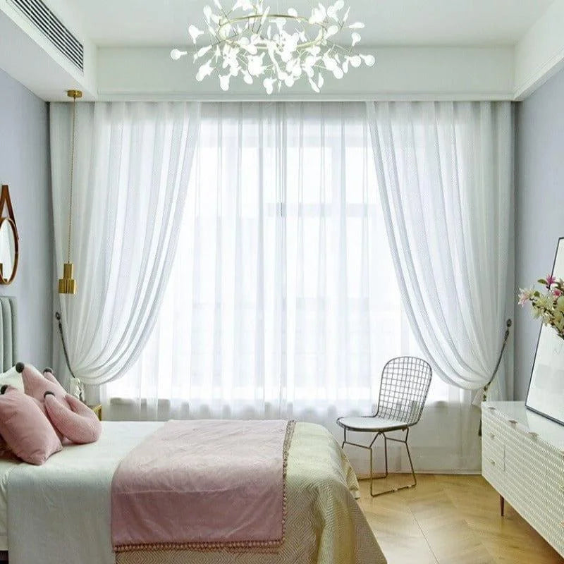 Chambre élégante avec un éclairage moderne et un lit confortable. Rideaux blancs laissant entrer la lumière naturelle, chaise design et décoration florale. Atmosphère apaisante et style contemporain idéal pour une chambre à coucher raffinée.