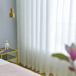 Rideaux blancs élégants dans une chambre lumineuse, accompagnés d'une table d'appoint moderne en verre avec des accents dorés, créant une atmosphère contemporaine et raffinée.
