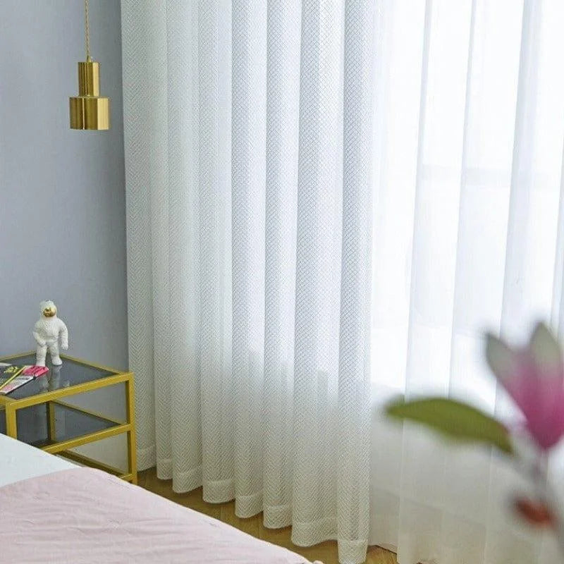 Rideaux blancs élégants dans une chambre lumineuse, accompagnés d'une table d'appoint moderne en verre avec des accents dorés, créant une atmosphère contemporaine et raffinée.