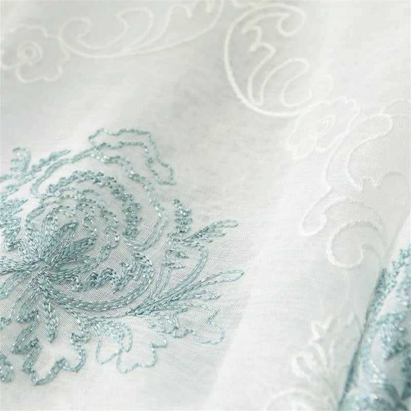 Détail d'une broderie élégante sur tissu, mettant en valeur un motif floral bleu subtil et raffiné, idéal pour la décoration intérieure et le design textile. Cette conception ajoute une touche de sophistication et de charme classique à tout espace de vie.