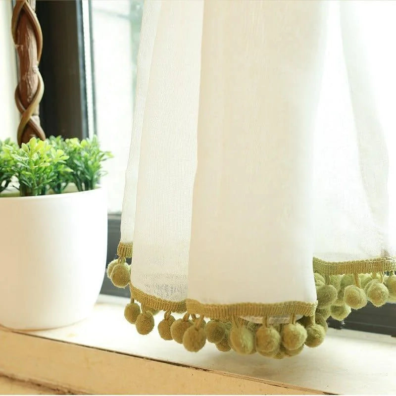 Voilage élégant avec pompons verts pour décoration intérieure, idéal pour ajouter une touche raffinée à votre salon ou chambre. Rideau léger suspendu près d'une fenêtre, accompagné d'une plante en pot sur une table, créant une ambiance chaleureuse et apaisante. Accessoire de maison moderne parfait pour filtrer doucement la lumière naturelle.