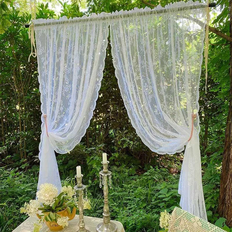 Rideaux élégants semi-transparents dans un jardin luxuriant. Décoration extérieure avec bougies et fleurs pour une ambiance romantique et naturelle. Idéal pour des événements en plein air ou un mariage champêtre.