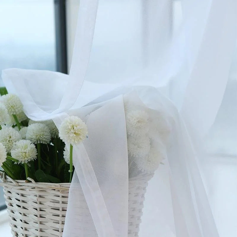 Voilage blanc élégant drapé autour d'un panier de fleurs blanches, idéal pour ajouter une touche de douceur et de romantisme à votre intérieur. Parfait pour décorer un salon lumineux ou une chambre apaisante, créant une atmosphère sereine et rafraîchissante.