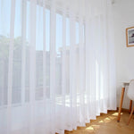 Voilage blanc élégant pour grande baie vitrée, apportant luminosité et intimité à votre espace de vie. Convient parfaitement aux intérieurs modernes et épurés. Installé dans un salon lumineux avec parquet clair, créant une atmosphère accueillante et chaleureuse.