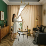 Femme élégante en robe blanche ouvrant un rideau voilage kaki dans un salon moderne chaleureux.
