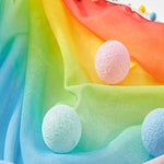 Écharpe aux couleurs de l'arc-en-ciel accompagnée de boules décoratives pastel. Accessoires décoratifs parfaits pour ajouter une touche de couleur vive à votre intérieur. Idéal pour la maison, offrant une atmosphère joyeuse et colorée.