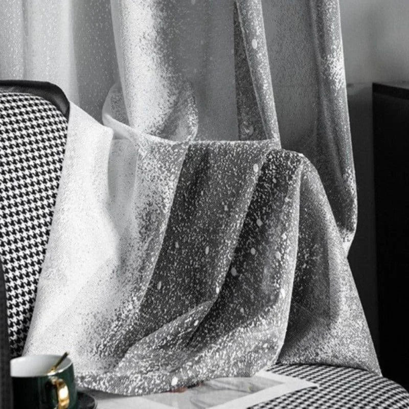 Rideau élégant à motifs argentés, drapé sur une chaise à motifs noirs et blancs. Ce rideau moderne ajoute une touche sophistiquée à tout intérieur, parfait pour créer une ambiance rafraîchissante et chic dans votre salon ou chambre à coucher. Idéal pour ceux qui cherchent à allier style et fonctionnalité dans leur décoration.