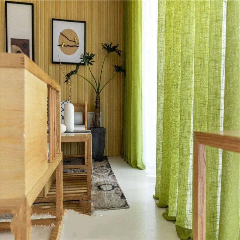 Salon moderne avec rideaux verts et mobilier en bois clair, créant une ambiance naturelle et accueillante. Plantes décoratives, lumière naturelle abondante, et décoration murale artistique ajoutent une touche d'élégance à la pièce. Idéal pour un intérieur contemporain et chaleureux.