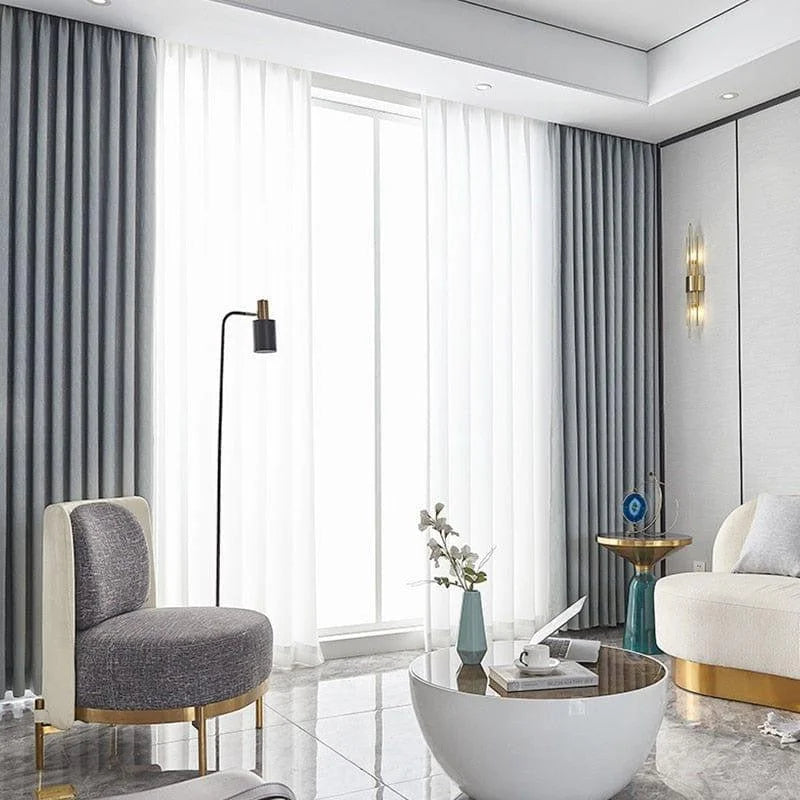 Salon moderne et élégant avec un canapé confortable et un fauteuil design, mettant en avant une table basse stylée sur un sol en marbre. Rideaux contemporains encadrant une grande fenêtre, créant une atmosphère lumineuse et accueillante. Ambiance raffinée, idéale pour un intérieur tendance.