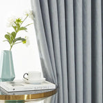 Rideau gris élégant pour salon moderne, ajout idéal pour une décoration intérieure raffinée. Accompagne parfaitement un vase décoratif bleu avec des fleurs blanches et une table basse chic, créant une atmosphère apaisante et stylée. Parfait pour ajouter une touche contemporaine à votre espace de vie.