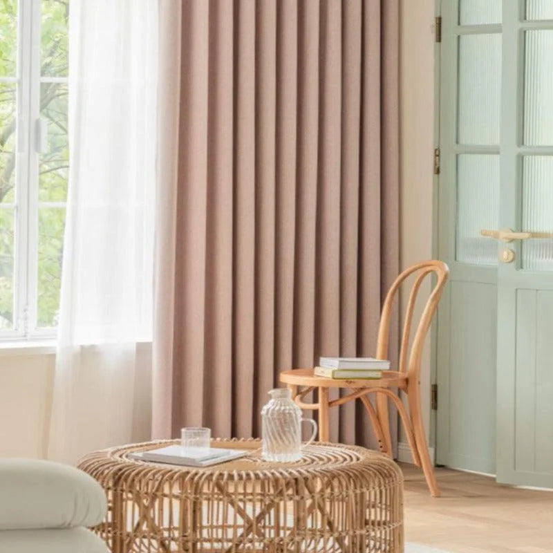 Rideaux opaques couleur taupe élégamment suspendus dans un salon moderne et lumineux, avec un mobilier en rotin et une chaise en bois clair pour une décoration intérieure chic et naturelle.