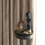 Draperies élégantes présentant un motif subtil, accompagnées d'une table d'appoint classique ornée d'un buste artistique et d'un cadre photo vintage. Décoration intérieure sophistiquée et intemporelle idéale pour un salon distingué.