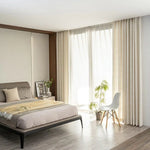 Chambre moderne avec lit élégamment décoré, rideaux lumineux, chaise design et plante, reflétant une atmosphère paisible et contemporaine. Décoration intérieure optimale pour améliorer votre espace de vie avec style et confort.