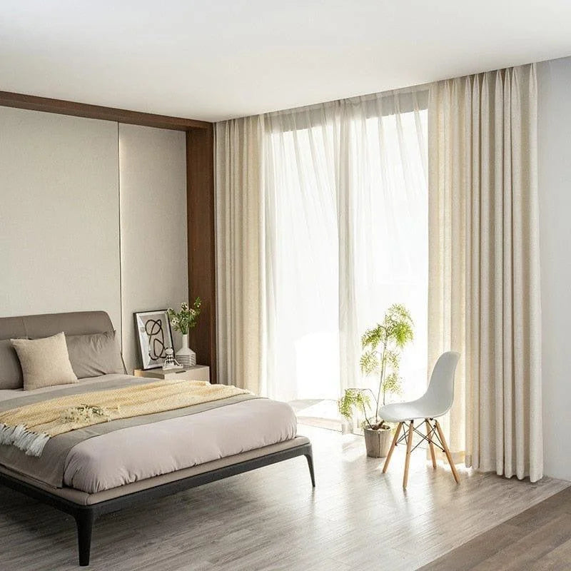 Chambre moderne avec lit élégamment décoré, rideaux lumineux, chaise design et plante, reflétant une atmosphère paisible et contemporaine. Décoration intérieure optimale pour améliorer votre espace de vie avec style et confort.