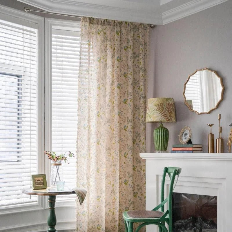 Rideau floral élégant suspendu dans un salon lumineux avec grandes fenêtres et stores en bois. Décoration intérieure moderne avec une table d'appoint, une lampe à poser verte sur la cheminée et un miroir au-dessus. Ambiance chaleureuse et cosy idéale pour un aménagement tendance et stylé de votre espace de vie.