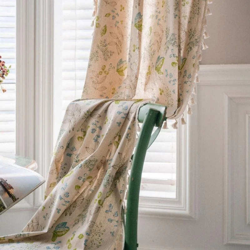 Rideau décoratif avec motifs floraux colorés, suspendu dans une salle lumineuse avec fauteuil et fenêtre à volets. Élément parfait pour ajouter une touche élégante et naturelle à tout intérieur. Accessoire idéal pour embellir votre espace avec des teintes douces et un design raffiné.