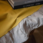 Vue rapprochée d'une table recouverte d'un tissu élégant avec des livres empilés sur le dessus, créant une ambiance chaleureuse et accueillante pour un espace de lecture ou de détente. Le contraste des couleurs entre le tissu et les livres apporte une touche moderne et raffinée à la décoration intérieure.