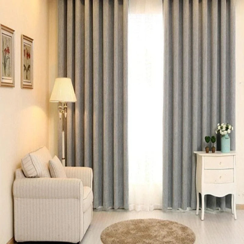 Salon élégant avec rideaux gris longs, fauteuil confortable, lampe sur pied, et table d'appoint blanche avec décoration florale. Design intérieur harmonieux et moderne pour un espace de vie accueillant.
