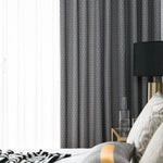 Rideaux modernes gris avec motifs, intégrés dans une chambre élégante. Décoration intérieure chic avec table de chevet dorée, lampe noire et coussins à motifs. Ambiance chaleureuse et sophistiquée pour une décoration de chambre raffinée.