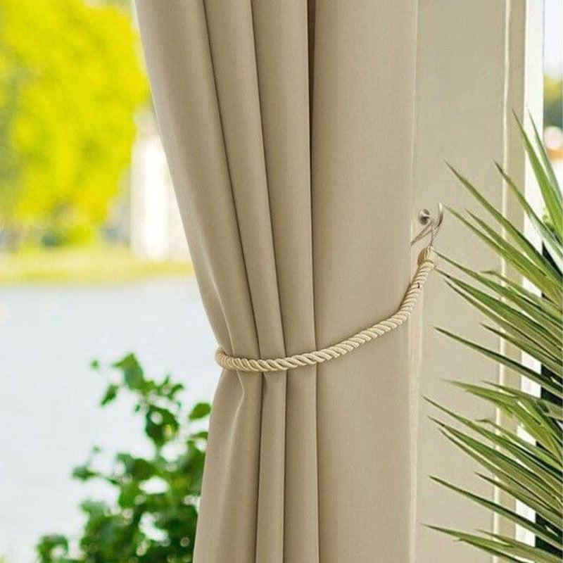 Attache rideau beige élégant avec embrasse en corde, idéale pour décorer le salon ou la chambre. Accessoire pratique offrant un style raffiné à votre intérieur. Fenêtre avec vue sur jardin et plante en premier plan.