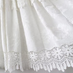 Élégant détail de broderie blanche sur le bas d'une robe, mettant en valeur des motifs floraux délicats avec une bordure en dentelle raffinée. Idéal pour les occasions spéciales, ce design apporte une touche sophistiquée et intemporelle à toute tenue.
