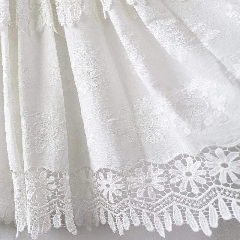 Élégant détail de broderie blanche sur le bas d'une robe, mettant en valeur des motifs floraux délicats avec une bordure en dentelle raffinée. Idéal pour les occasions spéciales, ce design apporte une touche sophistiquée et intemporelle à toute tenue.
