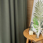 Rideau vert élégant pour décoration intérieure moderne, idéal pour ajouter une touche de sophistication à votre salon ou chambre. Accompagné d'une table en bois avec une affiche botanique et des bouquets de fleurs, créant une ambiance naturelle et apaisante. Solution parfaite pour un aménagement intérieur harmonieux.