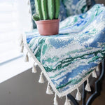 Nappe décorative à motifs bleus et verts avec franges, idéale pour ajouter une touche élégante à votre intérieur. Accompagnée d'un petit cactus en pot, cette nappe transforme votre espace en un lieu accueillant et moderne. Accessoire parfait pour les tables de salon ou de salle à manger.