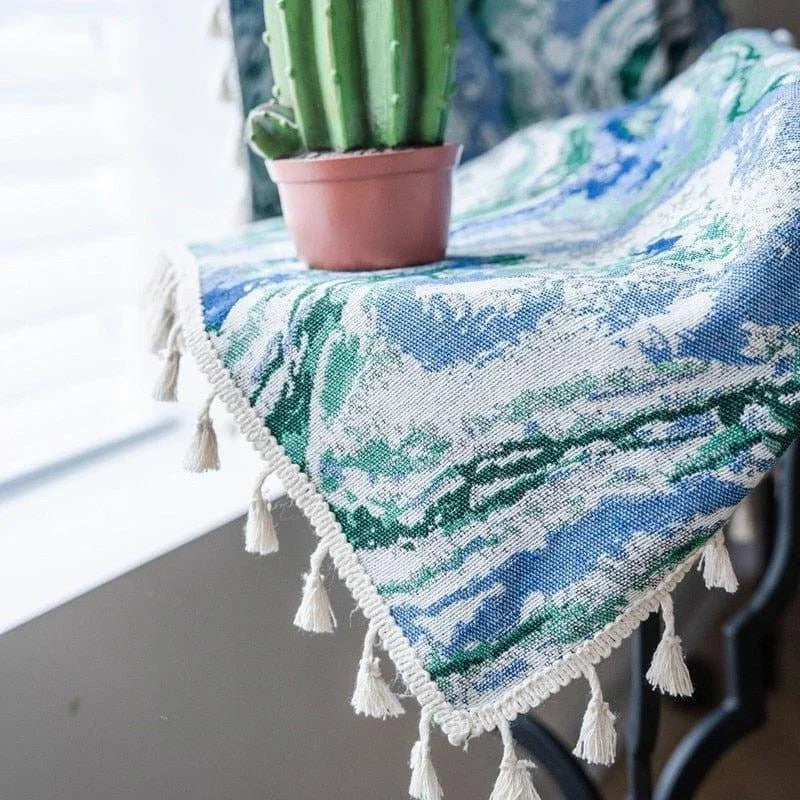 Nappe décorative à motifs bleus et verts avec franges, idéale pour ajouter une touche élégante à votre intérieur. Accompagnée d'un petit cactus en pot, cette nappe transforme votre espace en un lieu accueillant et moderne. Accessoire parfait pour les tables de salon ou de salle à manger.