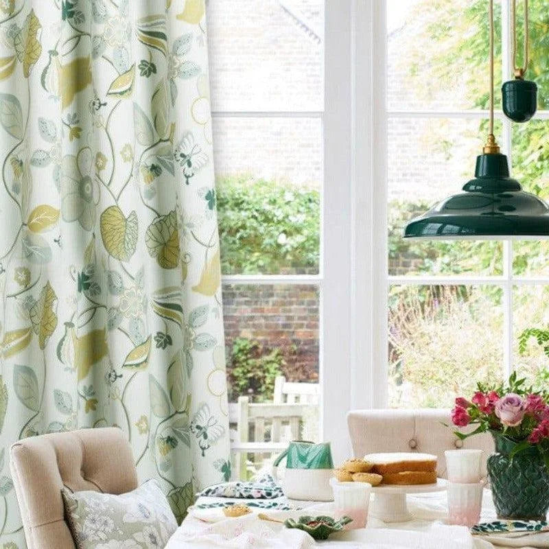 Rideaux à motifs floraux verts et jaunes, ajoutant une touche de fraîcheur et de nature à votre décoration intérieure, suspendus près d'une grande fenêtre laissant entrer la lumière naturelle. Parfait pour illuminer votre salle à manger ou salon, avec un style élégant et accueillant.