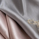Tissu élégant dans des tons argentés et roses, idéal pour la décoration intérieure ou la confection de vêtements chic. Les nuances subtiles apportent une touche sophistiquée. Accessoire en perles visible pour un ajout luxueux. Parfait pour les amateurs de design raffiné.