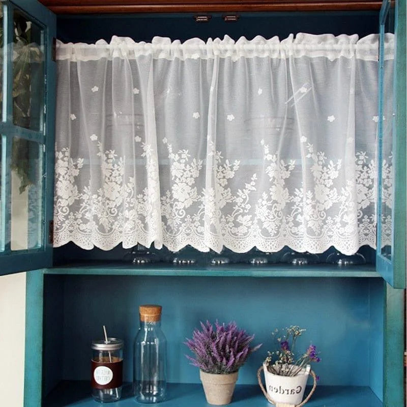 <img src="chemin/vers/image.jpg" alt="Rideau de fenêtre blanc avec motif floral élégant dans une armoire en bois bleu, déco intérieure chic avec plante lavande en pot et bouteilles décoratives" />