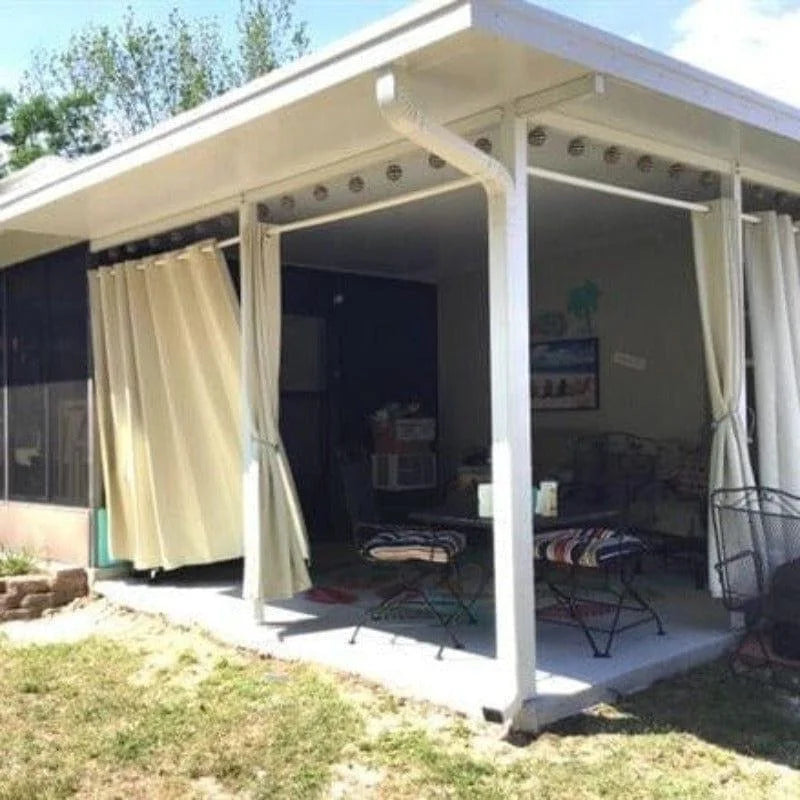 Véranda moderne avec rideaux ouverts située dans un jardin, offrant un espace ombragé et accueillant pour se détendre en plein air. Idéale pour profiter des journées ensoleillées tout en étant protégé du vent et des intempéries. Design épuré et pratique pour optimiser votre confort extérieur.