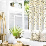Salon extérieur moderne avec un élégant rideau floral. Canapé confortable décoré de coussins à motifs géométriques. Atmosphère lumineuse et naturelle avec des plantes vertes en pot, idéale pour la détente.