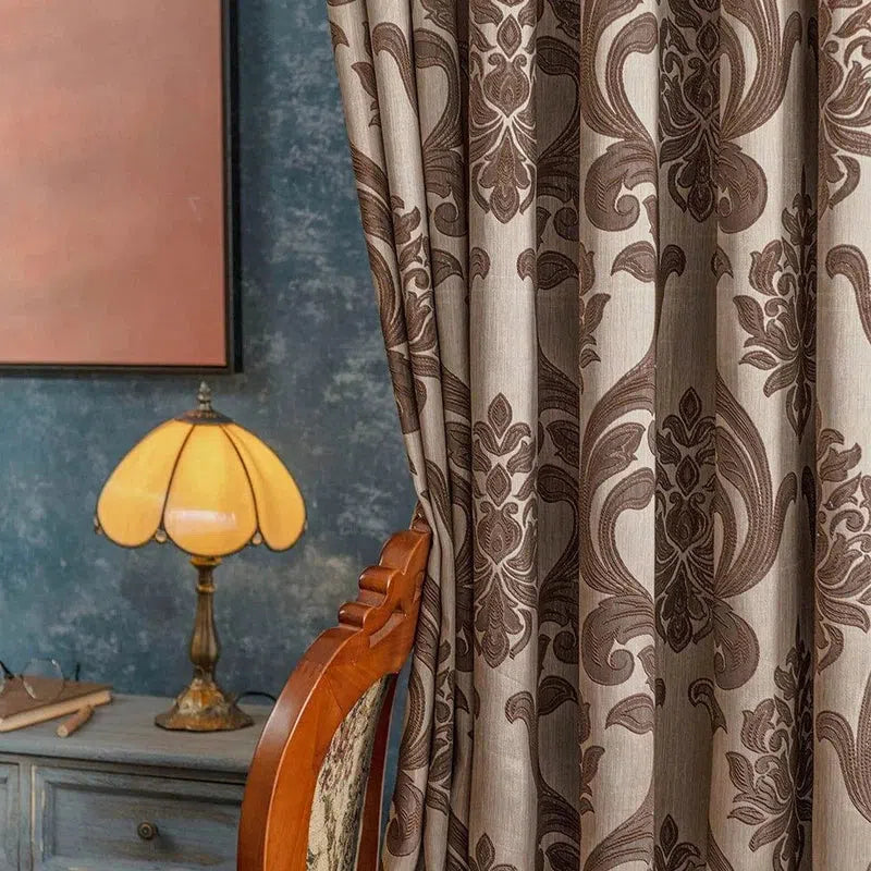 Rideau élégant avec motifs classiques, parfait pour une décoration intérieure raffinée. Accessoire idéal pour apporter une touche de sophistication à votre salon. Présenté dans un intérieur chaleureux avec une lampe vintage et un tableau subtil en arrière-plan.