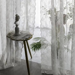 Rideaux élégants ornés de motifs floraux, apportant une touche de sophistication à votre intérieur. Décoration intemporelle idéale pour les salons ou chambres à coucher. Meuble d'appoint en bois avec sculpture décorative, ajoutant un charme artistique à la pièce. Plantes d'intérieur en arrière-plan, créant une ambiance naturelle et apaisante. Parfait pour ceux qui recherchent une décoration raffinée et un style classique dans leur maison.