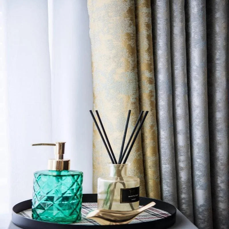 Distributeur de savon élégant vert avec détails dorés sur plateau décoratif, accompagné d'un diffuseur de parfum aux bâtons noirs, devant des rideaux raffinés dans un intérieur moderne. Idéal pour ajouter une touche de sophistication à votre salle de bain ou cuisine. Design chic et fonctionnel pour un espace accueillant.