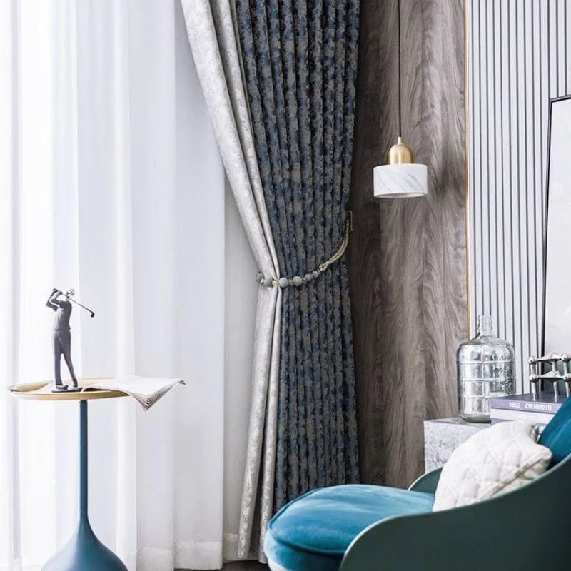 Rideaux élégants dans un salon moderne, créant une ambiance chic et raffinée. Ce décor met en valeur un fauteuil confortable avec une teinte bleue apaisante, une table d'appoint moderne avec une sculpture artistique, et un éclairage pendulaire qui apporte une touche sophistiquée à l'ensemble du design intérieur. Parfait pour améliorer l'esthétique de votre espace de vie.