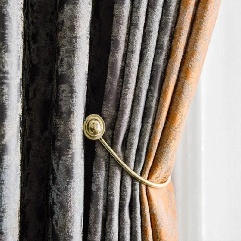Rideau élégant en tons de gris et orange, image présentant un tie-back doré accrochant le tissu en plis raffinés, parfait pour rehausser l'intérieur de la maison avec une touche de sophistication. Accessoire de décoration idéal pour un salon moderne.