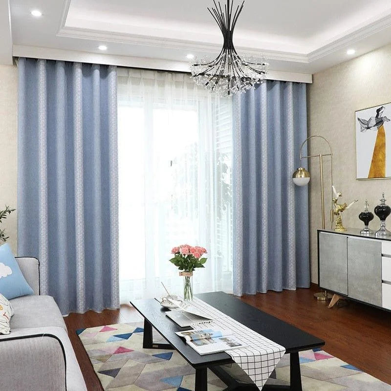 Rideaux bleu clair modernes pour salon, installation élégante devant une grande baie vitrée, offrant une ambiance lumineuse et sophistiquée. Décoration intérieure contemporaine avec canapé gris, table basse noire et tapis multicolore, idéale pour transformer votre espace de vie avec style. Lustre design et accessoires décoratifs ajoutent une touche de raffinement à votre maison.