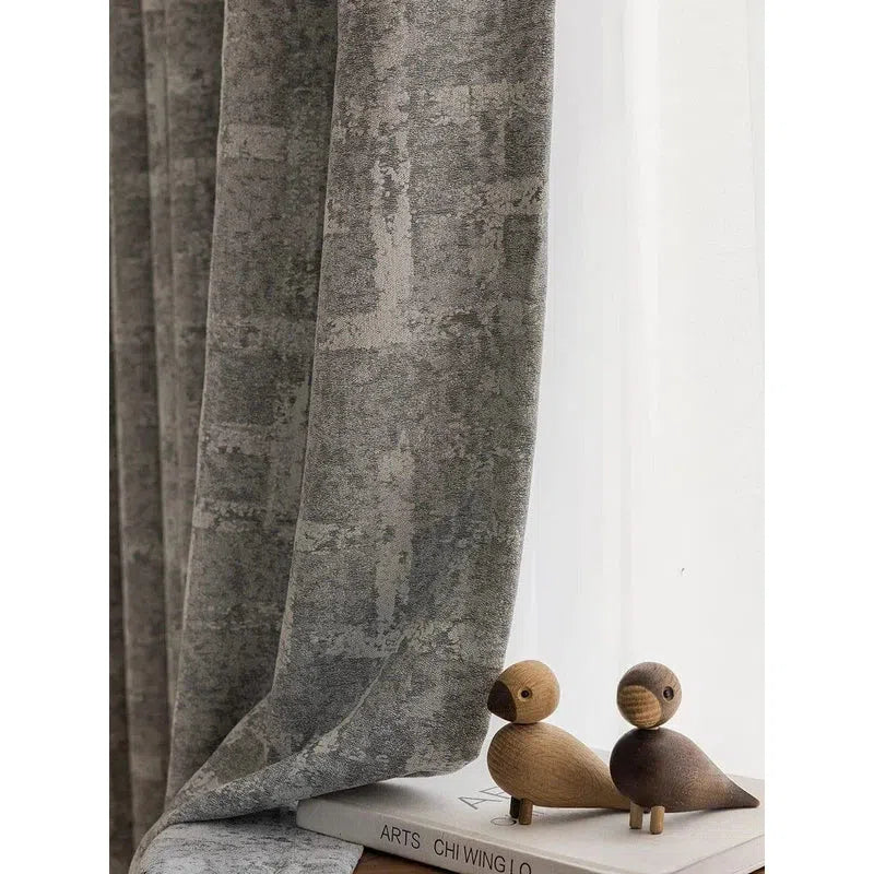Rideau élégant gris à motif texturé, idéal pour une ambiance moderne dans le salon ou la chambre. Complété par des objets décoratifs en bois sur une étagère, ce rideau ajoute une touche contemporaine et chaleureuse à votre intérieur. Parfait pour tamiser la lumière et apporter une touche de sophistication à votre décoration d'intérieur.