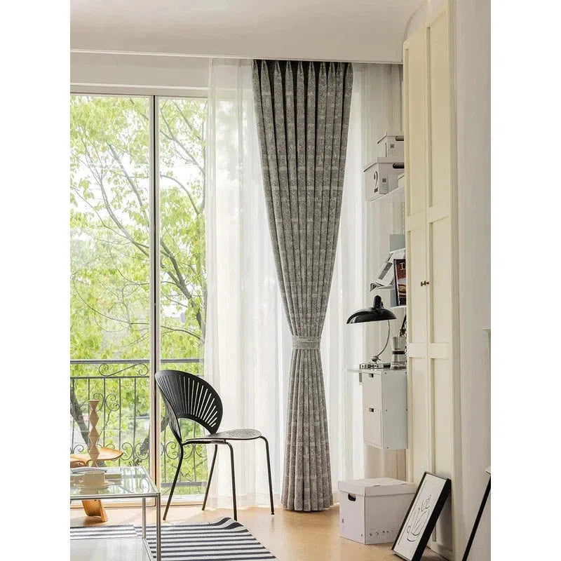 Rideau gris moderne et élégant installé dans un salon lumineux avec vue sur un balcon verdoyant. Ambiance cosy et contemporaine, idéale pour embellir votre intérieur tout en filtrant la lumière naturelle. Accessoire décoratif parfait pour une décoration intérieure raffinée.