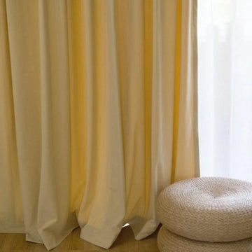 Rideaux élégants de couleur jaune pâle pour salon avec pouf tressé beige sur plancher en bois. Ambiance lumineuse et chaleureuse pour intérieur moderne.